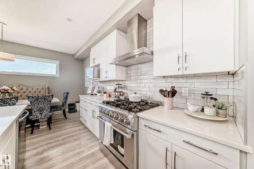 Modern kitchen featuring white cabinetry, light countertops, subway tile backsplash, stainless steel range with hood, and wood-finish flooring - 38 Prospect Place, Spruce Grove, AB - Indoor Photo Showing Kitchen With Upgraded Kitchen