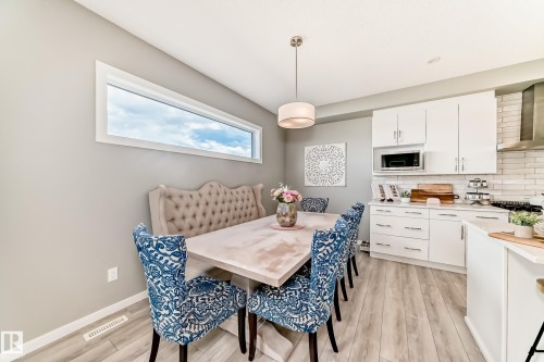 Open-concept kitchen and dining area featuring a linear window, wood-finish flooring, white cabinetry, a built-in microwave, and a stainless steel range hood - 38 Prospect Place, Spruce Grove, AB - Indoor Photo Showing Other Room