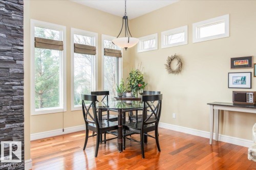Dining area featuring rich wood-finish flooring, a stone accent wall, and multiple large windows with natural light - 2413 Tegler Green, Edmonton, AB - Indoor Photo Showing Dining Room