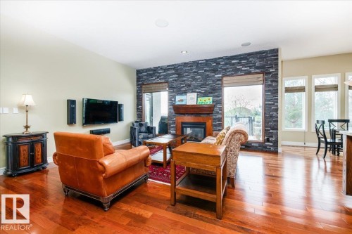 Living area featuring wood-finish flooring and a stone-clad accent wall with an integrated fireplace and wood mantel - 2413 Tegler Green, Edmonton, AB - Indoor Photo Showing Living Room With Fireplace