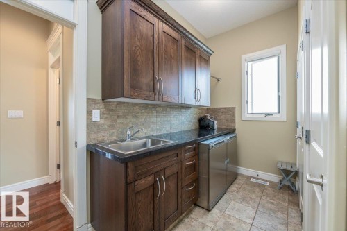 Utility area featuring dark wood-finish cabinetry, a stainless steel sink, and a dark stone-finish countertop - 2413 Tegler Green, Edmonton, AB - Indoor Photo Showing Kitchen