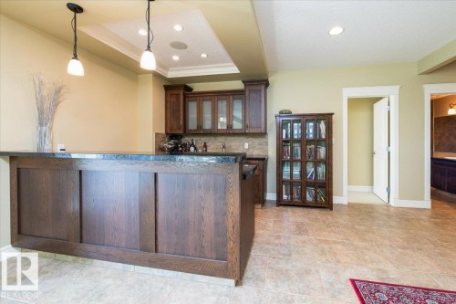 Built-in wet bar featuring dark wood cabinetry, a stone-look countertop, and pendant lighting - 2413 Tegler Green, Edmonton, AB - Indoor