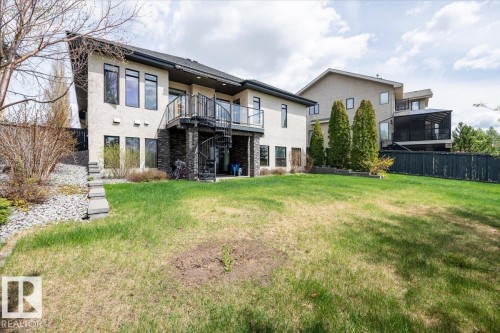 Expansive rear exterior featuring stucco siding, a stone accent foundation, a spiral staircase leading to a ground-level patio, and an upper-level balcony with glass railings - 2413 Tegler Green, Edmonton, AB - Outdoor