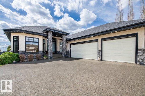 Contemporary stucco and stone exterior featuring a covered entry, two expansive garage doors, dark-framed windows, and a concrete driveway - 2413 Tegler Green, Edmonton, AB - Outdoor