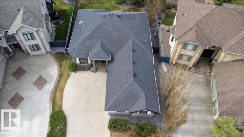 Spacious property featuring a dark grey shingled roof, light-colored concrete driveway, stone facade accents, and surrounding green landscaping - 2413 Tegler Green, Edmonton, AB - Outdoor