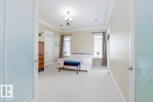 Spacious bedroom featuring light-toned carpeting, crown molding, a tray ceiling with a chandelier, and dual windows with blinds - 2413 Tegler Green, Edmonton, AB - Indoor Photo Showing Bedroom