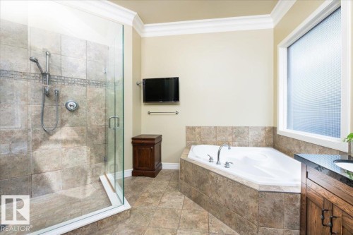 Tiled shower enclosure with glass surround, corner soaking tub with tiled base, and a vanity featuring a dark countertop and wood-finish cabinetry - 2413 Tegler Green, Edmonton, AB - Indoor Photo Showing Bathroom