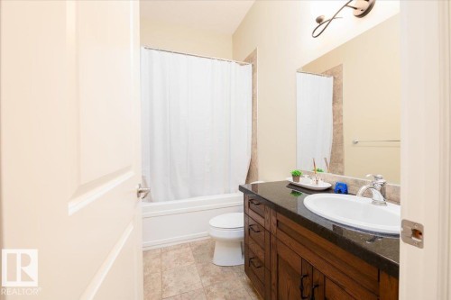 Bathroom featuring a white bathtub, ceramic tile flooring, a dark wood-finish vanity with a dark countertop, an oval undermount sink, and a wall-mounted light fixture - 2413 Tegler Green, Edmonton, AB - Indoor Photo Showing Bathroom