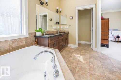 Spacious bathroom featuring an integrated soaking tub with chrome fixtures, a double vanity with dark wood-finish cabinetry, a dark countertop, and dual basins - 2413 Tegler Green, Edmonton, AB - Indoor Photo Showing Bathroom