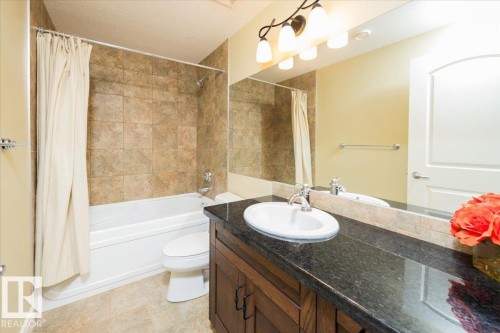 Bathroom vanity with an undermount sink and dark countertop, complemented by a large wall mirror and a decorative light fixture - 2413 Tegler Green, Edmonton, AB - Indoor Photo Showing Bathroom