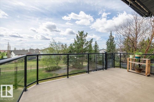 Spacious outdoor balcony with a concrete floor, black-framed glass railings, and mature trees providing natural screening - 2413 Tegler Green, Edmonton, AB - Outdoor With Exterior