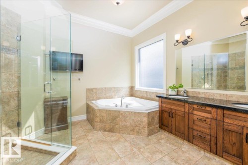 Spacious bathroom featuring a corner soaking tub, a large glass-enclosed shower, a dual-sink vanity with dark wood cabinetry and a black countertop, and neutral-toned tile flooring - 2413 Tegler Green, Edmonton, AB - Indoor Photo Showing Bathroom