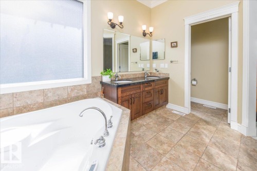 Bathroom featuring a built-in soaking tub with polished chrome fixtures, a large privacy window, and tiled flooring - 2413 Tegler Green, Edmonton, AB - Indoor Photo Showing Bathroom
