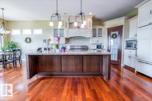 Kitchen featuring a large wood-paneled island with a speckled countertop, hardwood-finish flooring, white upper and lower cabinetry, built-in microwave, and a gas range - 2413 Tegler Green, Edmonton, AB - Indoor Photo Showing Kitchen