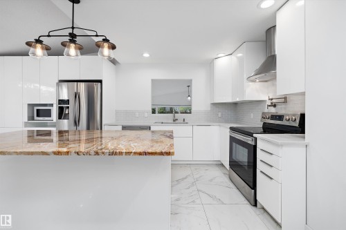 Kitchen featuring a large central island with a polished countertop, stainless steel appliances, white flat-panel cabinetry, a tile backsplash, and recessed lighting - 11525 37A Avenue Nw, Edmonton, AB - Indoor Photo Showing Kitchen With Upgraded Kitchen