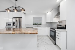 Kitchen featuring a large central island with a polished countertop, stainless steel appliances, white flat-panel cabinetry, a tile backsplash, and recessed lighting - 