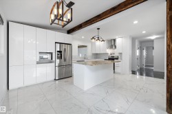 Modern kitchen featuring white cabinetry, stainless steel appliances, a center island with a stone countertop, and large format tile flooring - 