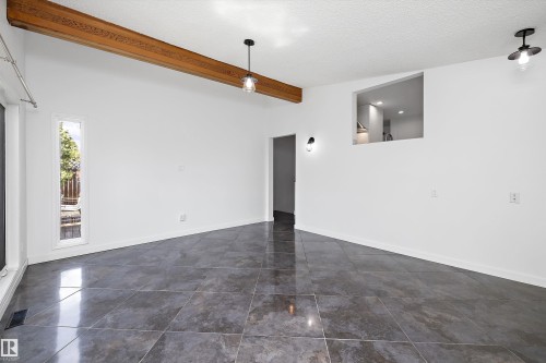 Spacious room featuring large format dark tile flooring, a prominent exposed wood beam, a pass-through opening, and multiple lighting fixtures - 11525 37A Avenue Nw, Edmonton, AB - Indoor Photo Showing Other Room