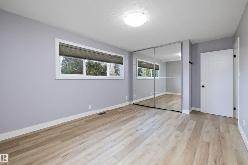 Room featuring wood-finish flooring, a wall of mirrored closet doors, and light gray painted walls - 11525 37A Avenue Nw, Edmonton, AB - Indoor Photo Showing Other Room