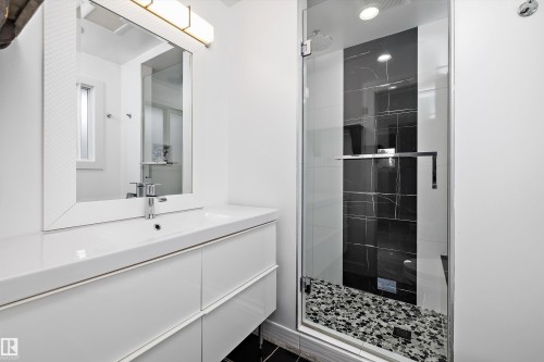 Contemporary bathroom featuring a spacious glass-enclosed shower, black marble-look tile accent wall, pebble tile shower floor, integrated rainfall showerhead, and a modern vanity with a rectangular basin - 11525 37A Avenue Nw, Edmonton, AB - Indoor Photo Showing Bathroom