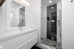 Contemporary bathroom featuring a spacious glass-enclosed shower, black marble-look tile accent wall, pebble tile shower floor, integrated rainfall showerhead, and a modern vanity with a rectangular basin - 