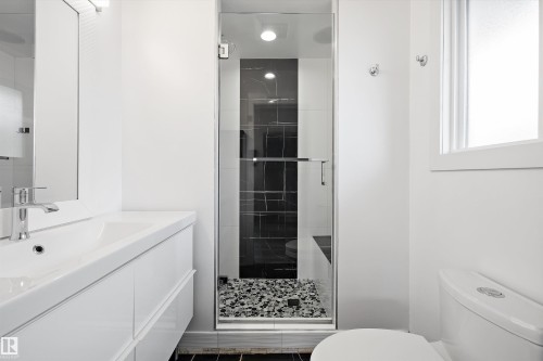 Modern bathroom featuring a glass-enclosed shower with dark tile surround and river rock flooring - 11525 37A Avenue Nw, Edmonton, AB - Indoor Photo Showing Bathroom