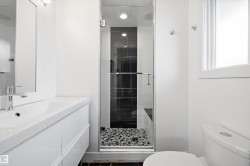Modern bathroom featuring a glass-enclosed shower with dark tile surround and river rock flooring - 