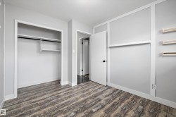Spacious room featuring wood-finish flooring, light grey walls with white trim, and a built-in closet with shelving and hanging rod - 