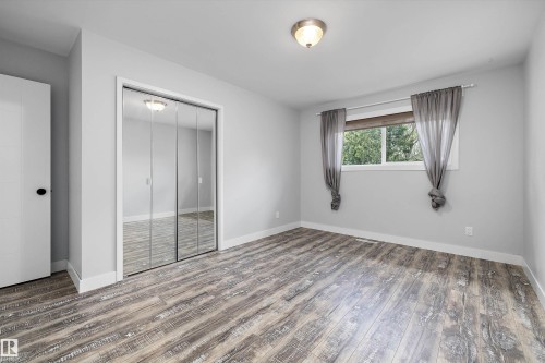 Spacious room featuring wood-finish flooring, a large window, mirrored closet doors, and recessed lighting - 11525 37A Avenue Nw, Edmonton, AB - Indoor Photo Showing Other Room