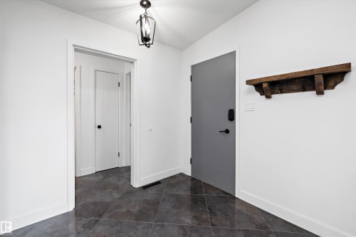 Entryway featuring dark gray tile flooring, crisp white walls, a black metal lantern-style ceiling fixture, a solid gray door with matte black hardware, and a rustic wood wall shelf - 11525 37A Avenue Nw, Edmonton, AB - Indoor Photo Showing Other Room