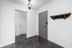 Entryway featuring dark gray tile flooring, crisp white walls, a black metal lantern-style ceiling fixture, a solid gray door with matte black hardware, and a rustic wood wall shelf - 
