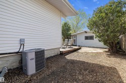Rear exterior with white vinyl siding, a gravel-covered ground, and a visible HVAC unit - 