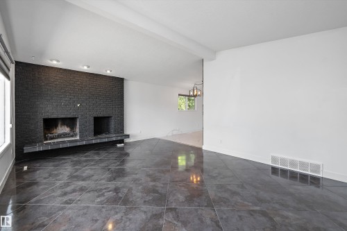 Spacious interior featuring large format dark grey tile flooring, a prominent black brick fireplace with a raised hearth, and recessed lighting - 11525 37A Avenue Nw, Edmonton, AB - Indoor Photo Showing Other Room With Fireplace