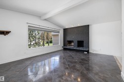Spacious room featuring vaulted ceilings with exposed beams, large format tile flooring, a black brick fireplace with two fireboxes, recessed lighting, and a wide picture window with roller shade - 