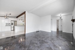 Spacious open-concept interior featuring large format tile flooring and a modern kitchen with high-gloss white cabinetry and stainless steel appliances - 