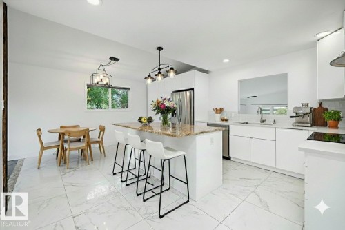 Bright kitchen featuring white cabinetry, a large center island with a stone countertop, stainless steel refrigerator, and integrated cooktop - 11525 37A Avenue Nw, Edmonton, AB - Indoor Photo Showing Kitchen