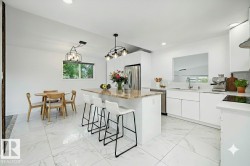 Bright kitchen featuring white cabinetry, a large center island with a stone countertop, stainless steel refrigerator, and integrated cooktop - 