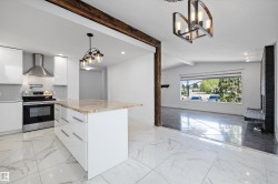 Bright kitchen with a spacious island featuring a stone-finish countertop, sleek white cabinetry, and stainless steel appliances including a range and range hood - 