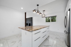 Kitchen island featuring a stone countertop, white cabinetry with horizontal hardware, and two pendant light fixtures - 