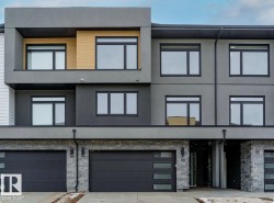 Contemporary multi-story exterior featuring a grey stucco facade, black-framed windows, and stone veneer accents - 