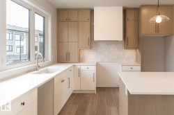 Modern kitchen featuring a large window, light wood-finish and white cabinetry, quartz countertops, a tile backsplash, and wood-finish flooring - 
