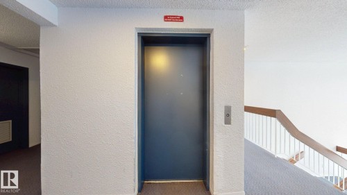 Central elevator access with a dark gray door and a stainless steel call panel - 402 2624 Millwoods East Road E, Edmonton, AB - Indoor Photo Showing Other Room