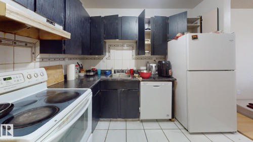 Kitchen featuring dark cabinetry, white tile flooring, a white range, a white dishwasher, and a white refrigerator - 402 2624 Millwoods East Road E, Edmonton, AB - Indoor Photo Showing Kitchen
