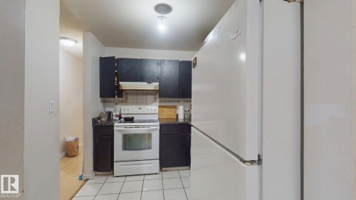 Kitchen featuring dark cabinetry, white appliances, tile flooring, and recessed lighting - 402 2624 Millwoods East Road E, Edmonton, AB - Indoor Photo Showing Kitchen