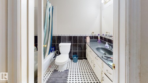 Bathroom featuring black and white mosaic floor tile, a white toilet, and a vanity with an integrated sink and cabinet storage - 402 2624 Millwoods East Road E, Edmonton, AB - Indoor Photo Showing Bathroom