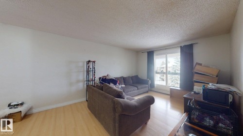 Expansive living area featuring light wood-finish flooring, white walls, and a large window with black curtain rods - 402 2624 Millwoods East Road E, Edmonton, AB - Indoor