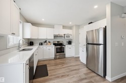 Contemporary kitchen featuring white cabinetry, stainless steel appliances, light-toned wood-finish flooring, recessed lighting, and a window with blinds - 