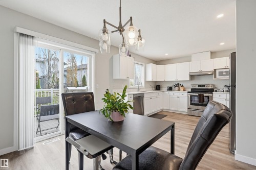 Modern kitchen featuring white cabinetry, stainless steel appliances, and light wood-finish flooring - 11 3380 28A Avenue Nw, Edmonton, AB - Indoor Photo Showing Dining Room