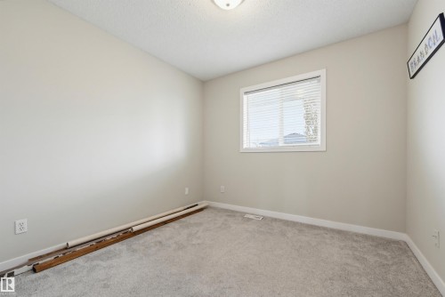 Neutral-toned room featuring a single window with horizontal blinds, light gray wall-to-wall carpeting, white baseboards, and a semi-flush mount ceiling light fixture - 11 3380 28A Avenue Nw, Edmonton, AB - Indoor