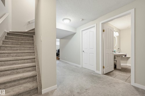 Carpeted staircase with a white handrail, leading to a hallway with light gray walls and recessed lighting - 11 3380 28A Avenue Nw, Edmonton, AB - Indoor